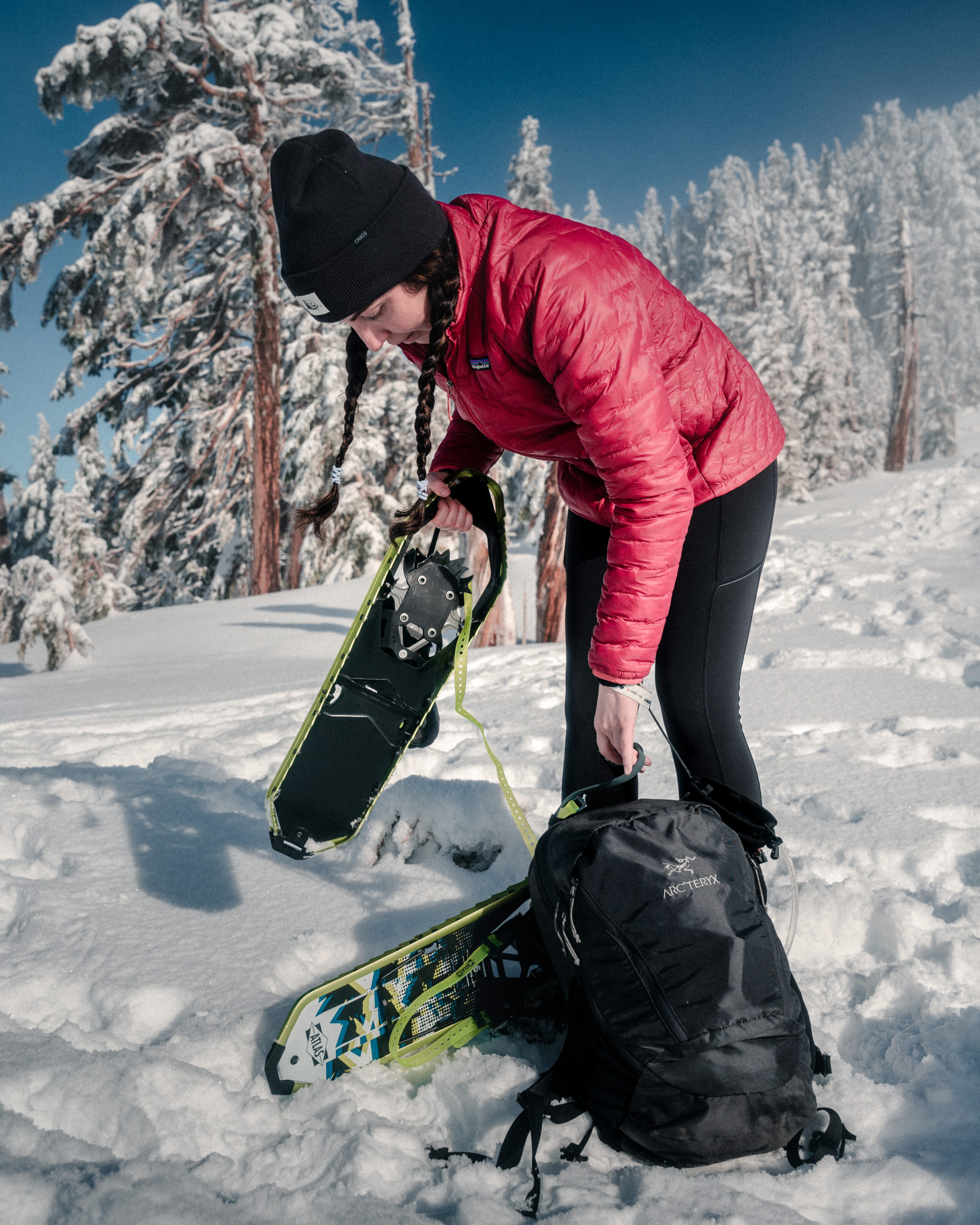 A woman unpacking snowshoes from her backpack while hiking. Photography by Michael Frymus